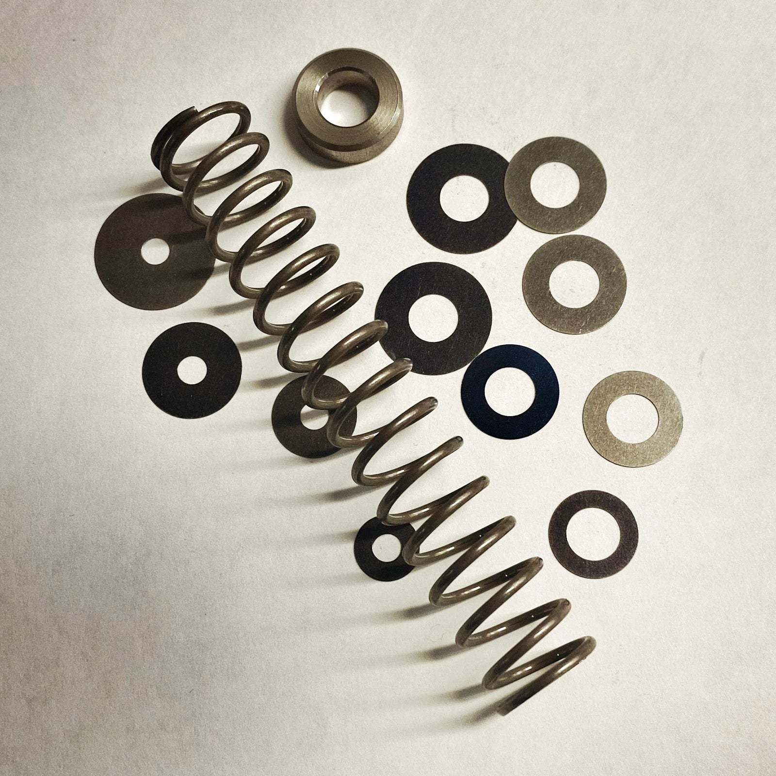 A set of metal parts including springs and washers likely for a bicycle fork damper tune kit.