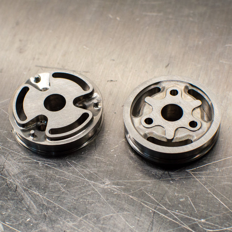 Two metal pistons are shown on a metallic surface, which appear to be part of a shock absorber assembly.