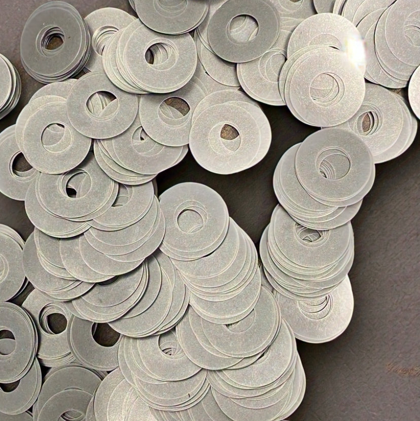 A pile of silver mountain bike valving shims spread out on a surface.