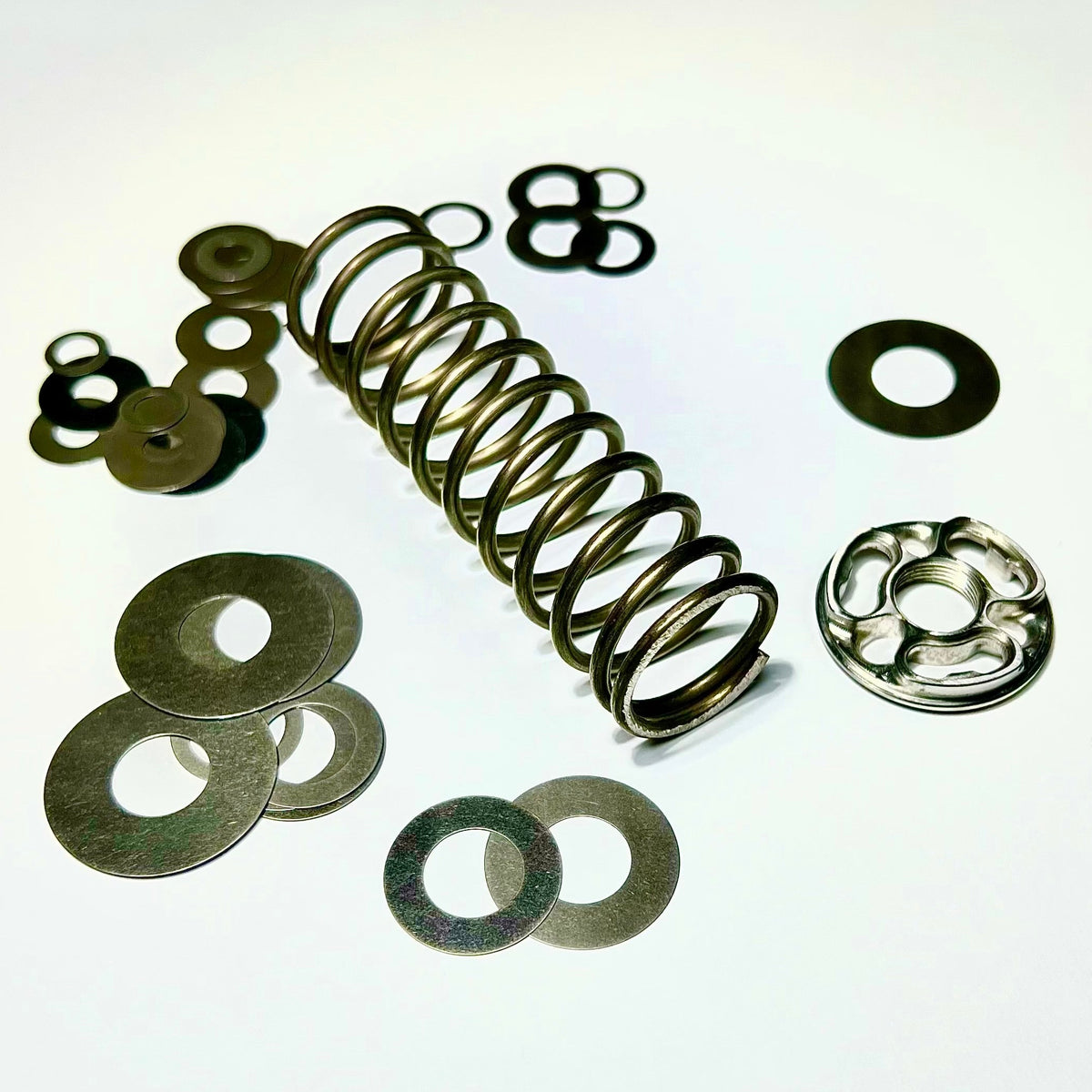A collection of metal components including a coiled spring and various washers, typically used for bicycle suspension systems.