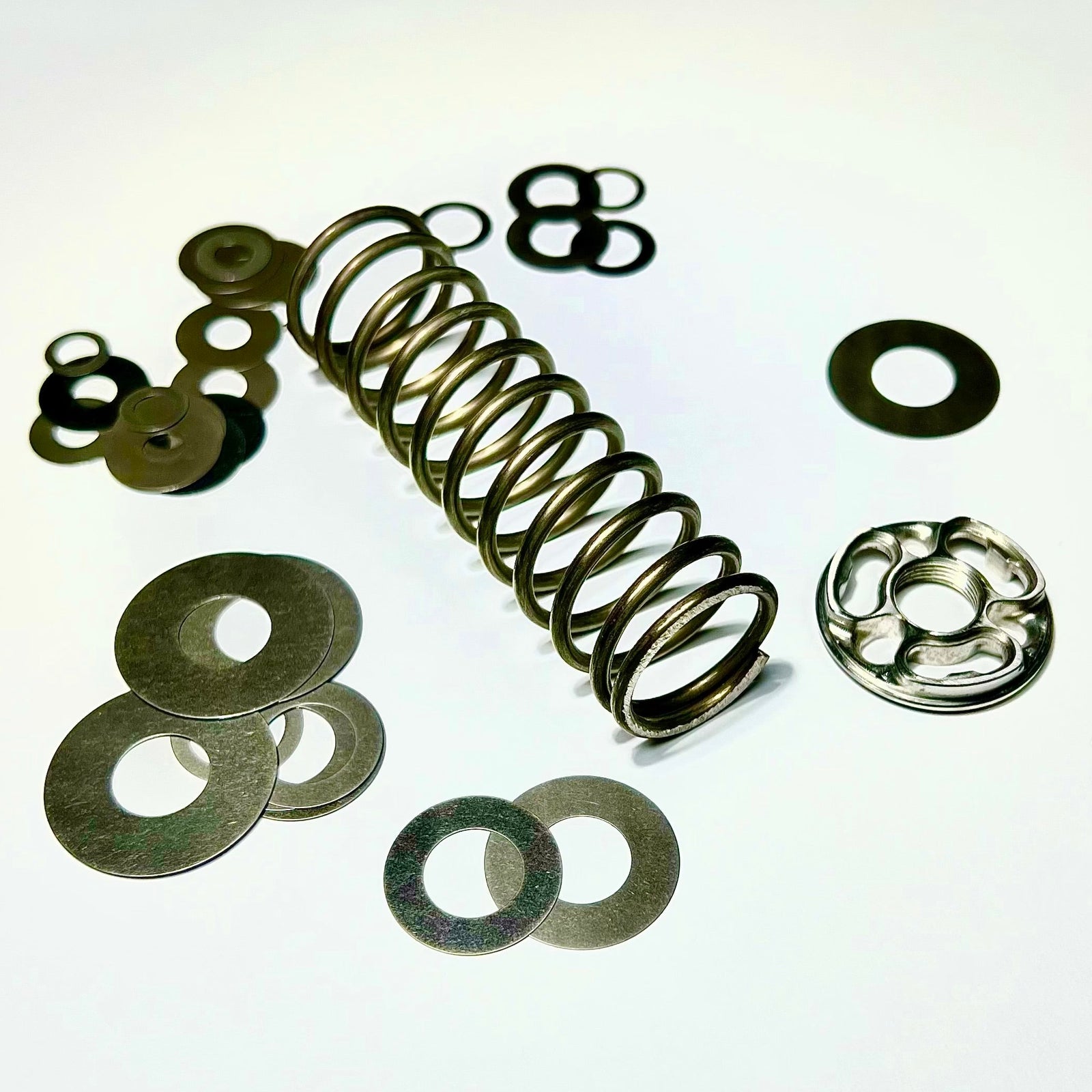 A collection of metal components including a coiled spring and various washers, typically used for bicycle suspension systems.