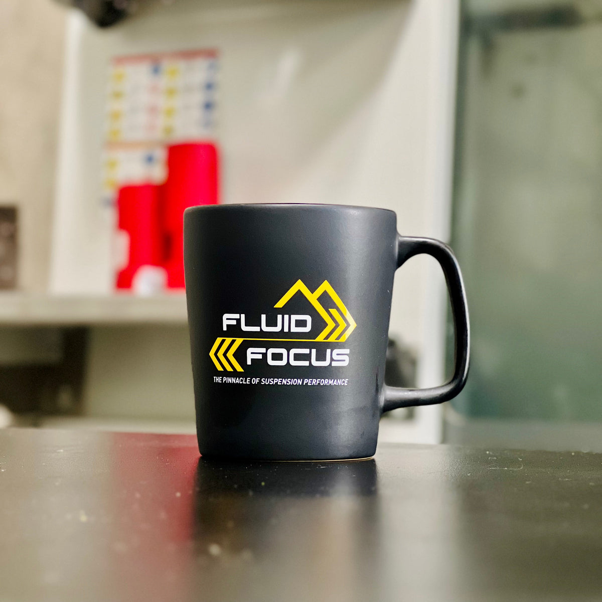 Black mug with 'Fluid Focus' logo on a counter in a kitchen setting