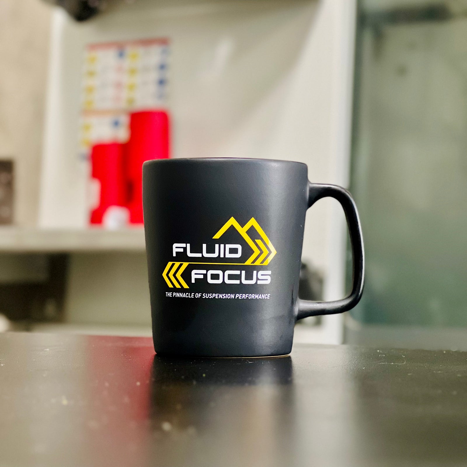 Black mug with 'Fluid Focus' logo on a counter in a kitchen setting