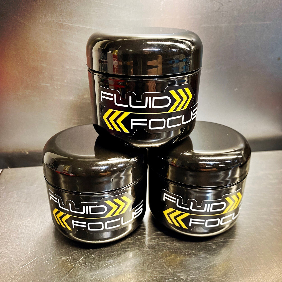 Three containers of Fluid Focus Suspension Ointment with black lids and yellow labeling, stacked on top of each other.